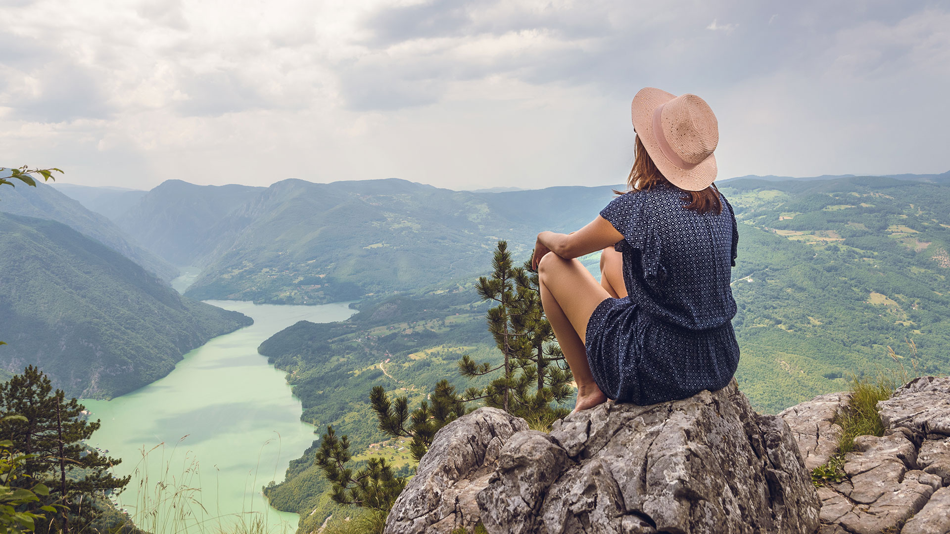 A young woman on a mountain top overlooking a river flowing between the mountains
